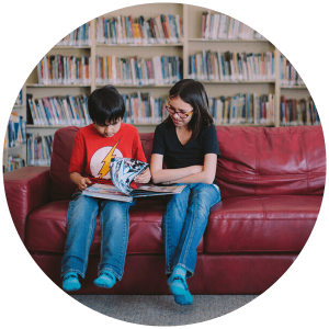 Chase and Nadine read a book on a couch in a library.