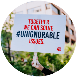 A hand holds up a sign that reads ``Together we can solve #unignorable issues.``