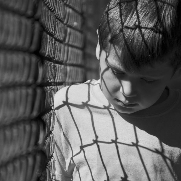 boy looking serious leaning against a fence