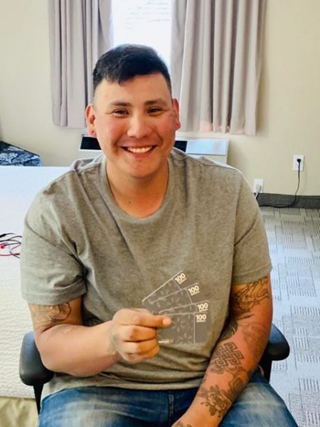 Brendon sitting in char, smiling, holding gift cards from wal-mart