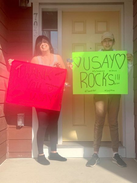 Two girls standing at a front door holding signs that read: USAY Rocks.
